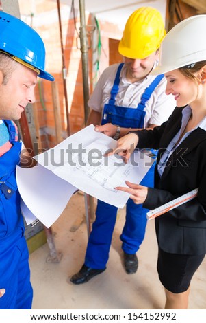 Construction site team or architect and builder or worker with helmets controlling or having discussion of plan or blueprint