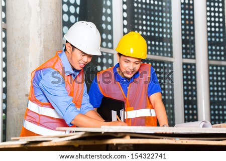 Chinese architect and supervisor point on building site on a construction plan