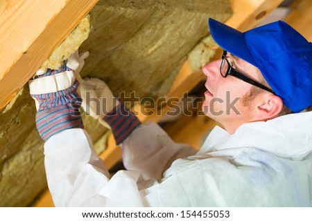 Worker in overall is setting thermal insulating material with gloves in the roof