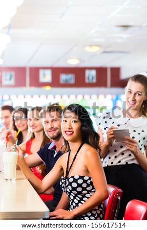 Friends or couples eating fast food and drinking milk shakes on bar in American fast food diner, the waitress is taking orders