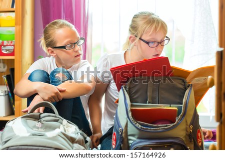 Girls or Sisters doing homework together and packing bags for school with text books next day