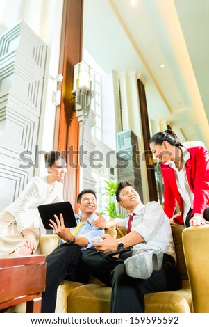 Group of four Asian Chinese businesspeople meeting for small team discussion in luxurious hotel lobby, there are documents on a tablet computer