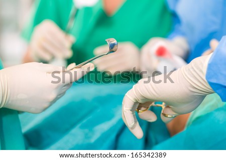 Hospital - doctor surgery team in the operating room or theater of clinic operating on patient, perhaps it is an emergency, assistant holding a cotton swap forceps