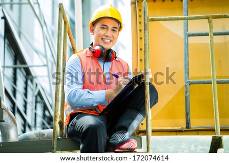 Asian Indonesian construction worker with helmet and safety vest on a building or industrial site in Asia