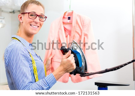Female cleaner in laundry shop or textile dry-cleaning ironing jacket by hand with iron