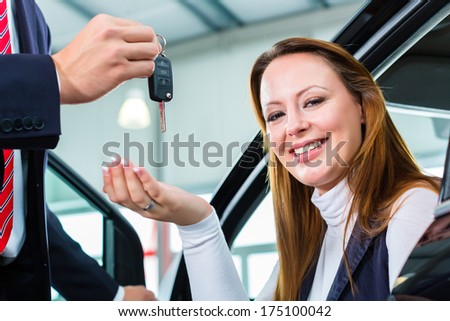Seller or car salesman and female client or customer in car dealership presenting the interior decoration of new and used cars in the showroom and hands over the car keys