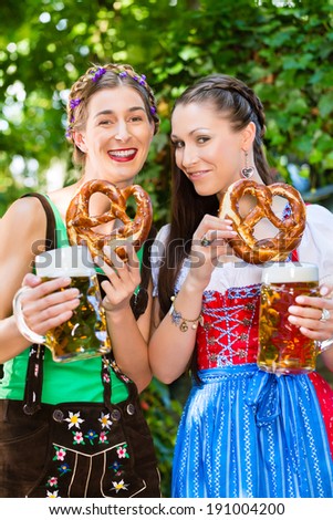 In Beer garden - female friends in Tracht, and Dirndl drinking a fresh beer and eating pretzel in Bavaria, Germany
