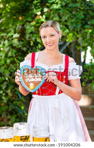Young woman in traditional Bavarian clothes or tracht with a gingerbread souvenir heart in beergarden on Oktoberfest