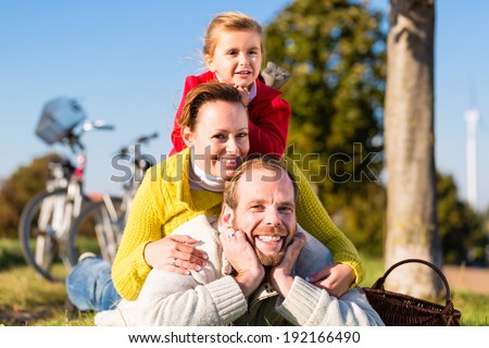 Family with mother, father and daughter having break on family trip with bicycle or cycle in park