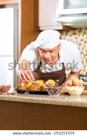 Asian man baking homemade cup cake muffins in his kitchen for dessert