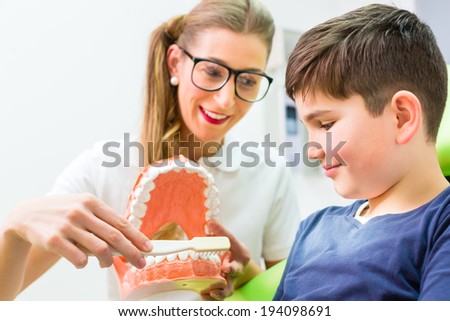 Female dentist explaining boy cleaning tooth with toothbrush on model