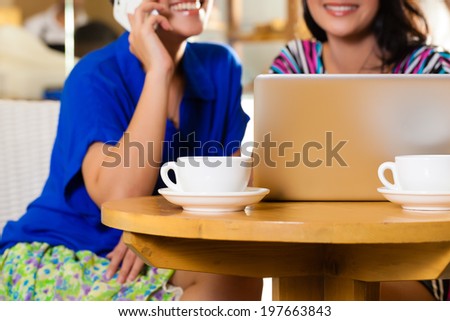 Asian female friends enjoying her leisure time in a cafe, drinking coffee or cappuccino and working on a laptop computer