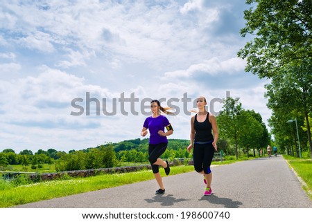 Urban sports - two women or female friends running together for better fitness in the city park on a cloudy summer day