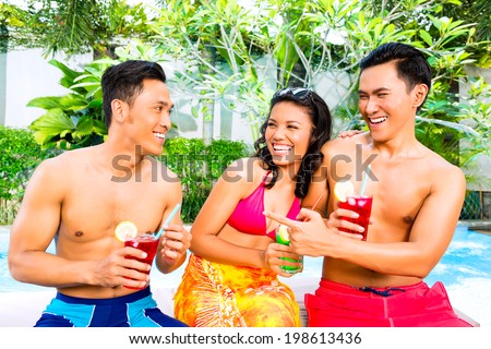 Asian friends drinking fancy cocktails at hotel or club pool
