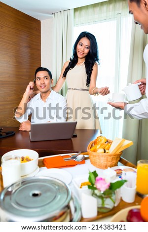 Asian room service waiter serving breakfast in hotel room