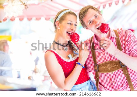 Couple visiting together Bavarian fair in national costume eating  candy apple