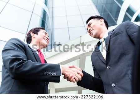 Asian business men outside in front of tower building shaking hands