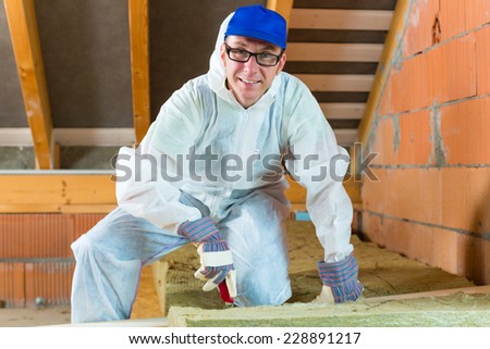 Worker in overall is cutting insulating material with gloves and knife
