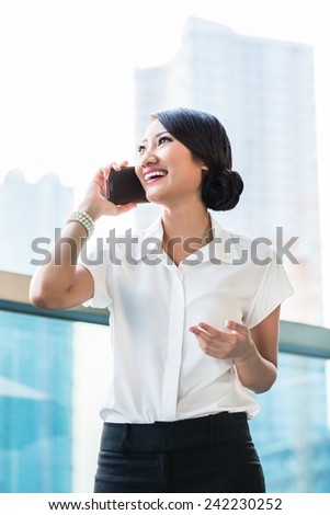 Chinese business woman using phone on terrace in front of city skyline