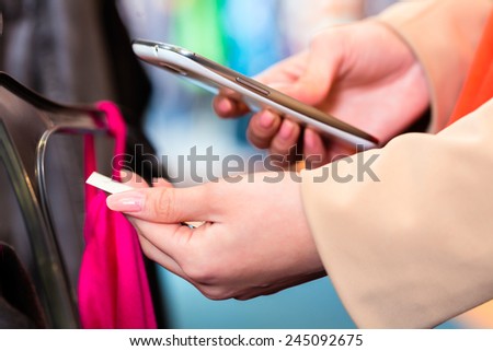 Woman shopping in boutique or fashion store comparing prices with mobile phone scanning the price tag
