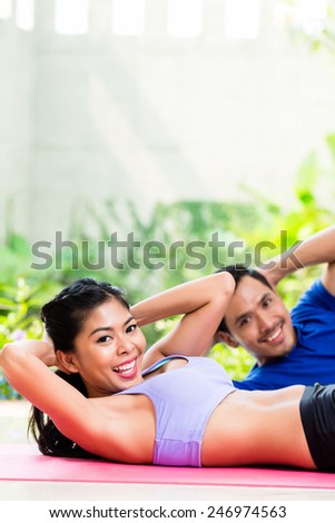 Asian fitness couple, man and woman, doing sit-up in tropical home