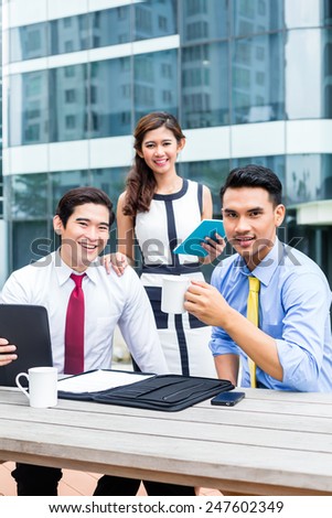 Asian business woman and men working outside on computer drinking coffee