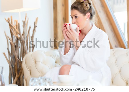 Woman in bath robe drinking tea in wellness spa relaxation room