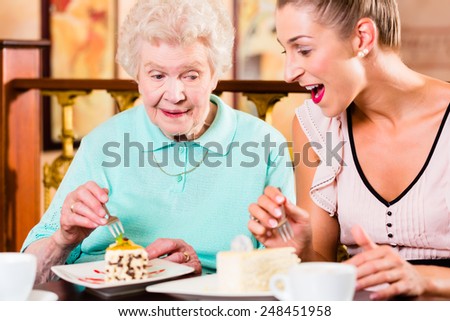 Senior woman and granddaughter drinking coffee and eating cake in cafe