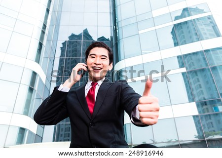 Asian businessman telephoning with smartphone in front of tower building