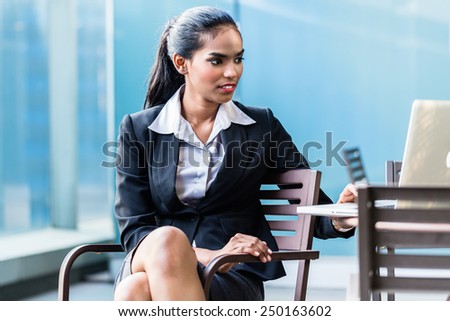 Indian Business woman working with laptop sitting on terrace in front of city skyline