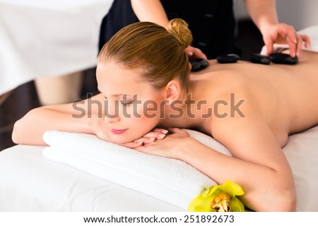 Woman in wellness beauty spa having hot stone massage, looking relaxed