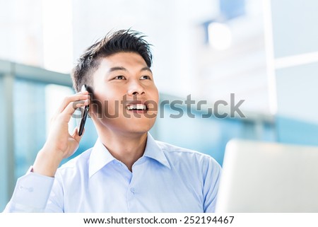 Chinese businessman using phone sitting in front of city skyline