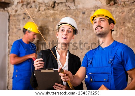 Builder and architect discussing on construction site, he is holding a folding rule pointing with it