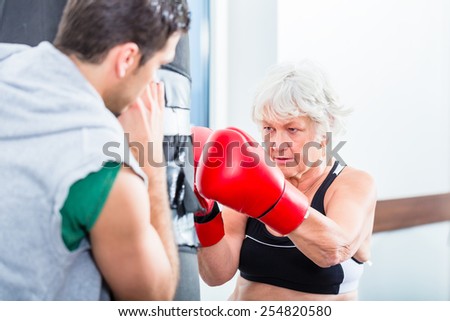 Senior woman with trainer in boxing sparring hitting sandbag