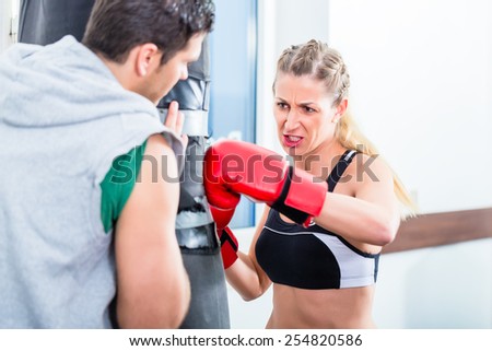 Young woman with trainer in boxing sparring hitting sandbag