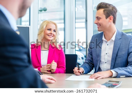Couple buying car at dealership and signing sales contract with salesman