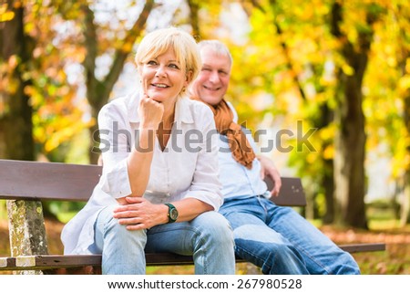 Senior woman and man sitting on part bench in fall