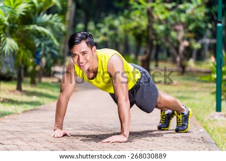 Strong Asian man doing sport push-up in park looking at camera