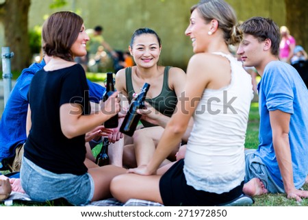 Students in park drinking beer and talk having picnic at river