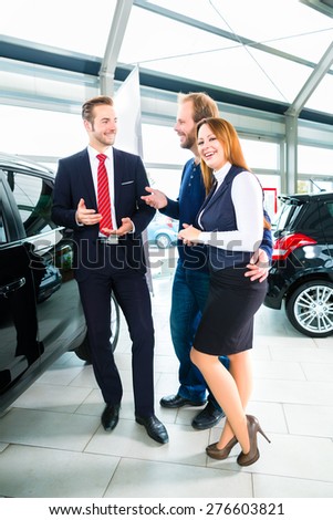 Seller or car salesman and clients or customers in car dealership presenting the interior decoration of new and used cars in the showroom