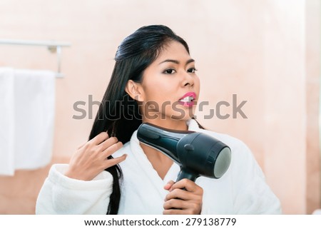 Asian woman in bathroom drying hair with blow dryer