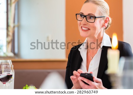 Woman in restaurant on business lunch checking mails on phone
