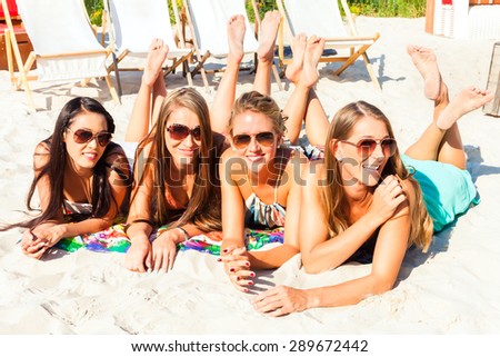 Four woman lying on beach sand, tanning in the sun
