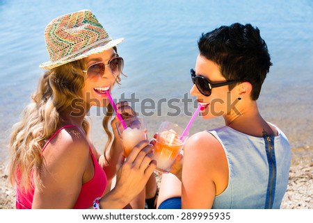 Women drinking cocktails at beach on swimming lake in sand