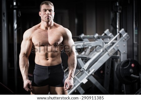 Strong man doing bodybuilding in gym standing in front of a dumbbell rack