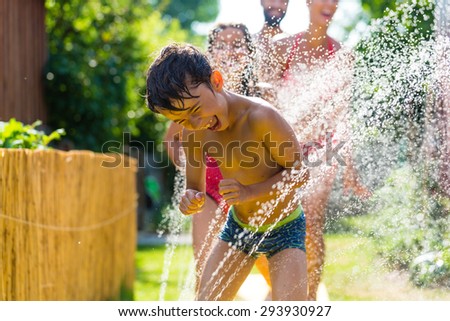 Family cooling down with sprinkler in garden, lots of water splashing around