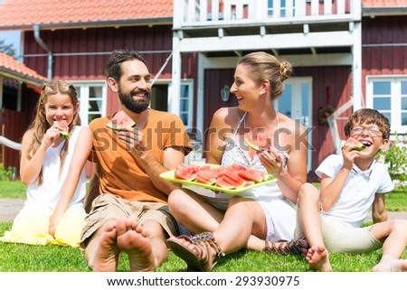 Family sitting in grass in front of house eating water melon to refresh in summer