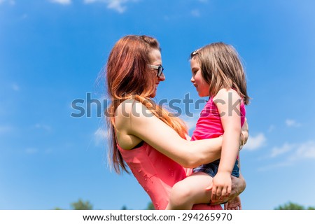Mother carrying daughter on her arm under a clear blue summer sky