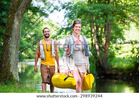 Man and woman carrying canoe to forest river