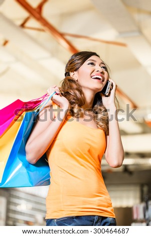 Asian young woman in fashion store or shop talking on phone telling her friends about the purchase she made